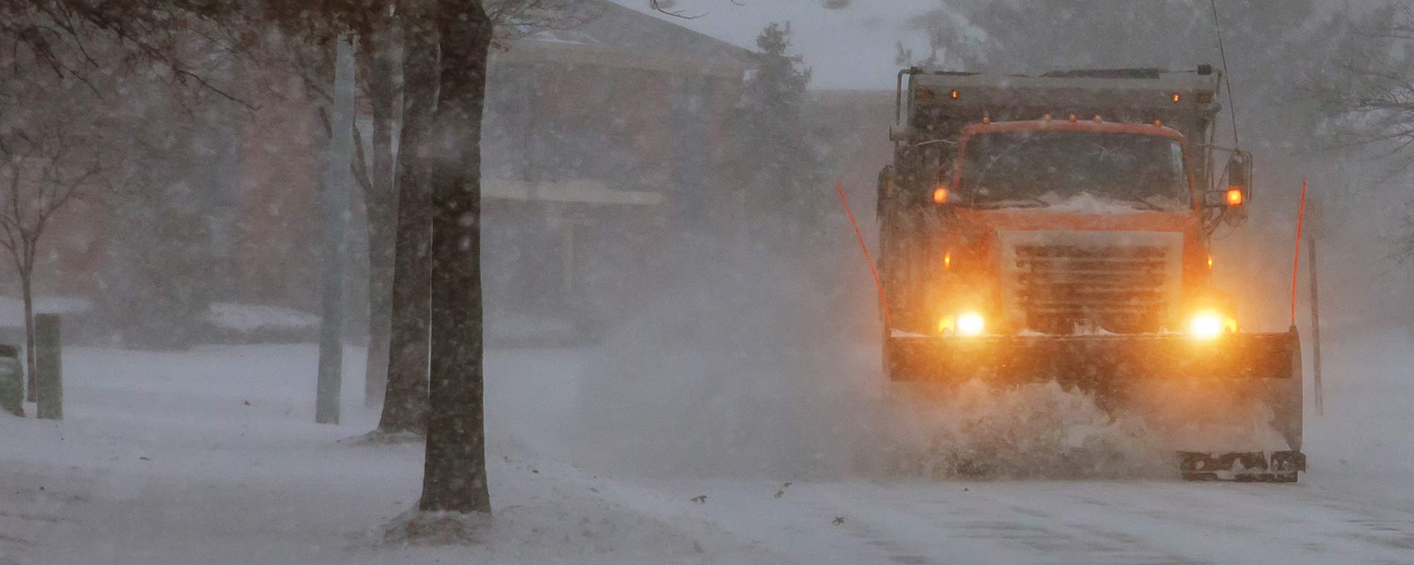 distance shot of snow plow and plow headlights clearing road in snow storm